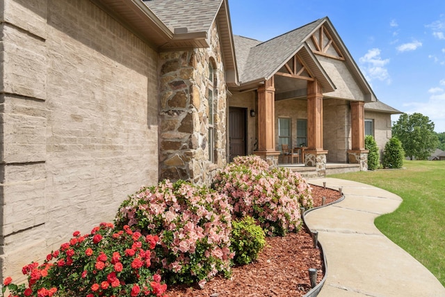 property entrance with a yard, stone siding, covered porch, and roof with shingles