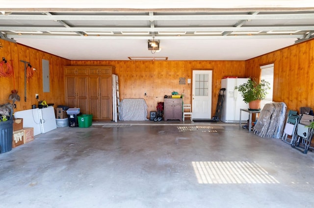 garage featuring wood walls, a garage door opener, electric panel, and white refrigerator with ice dispenser