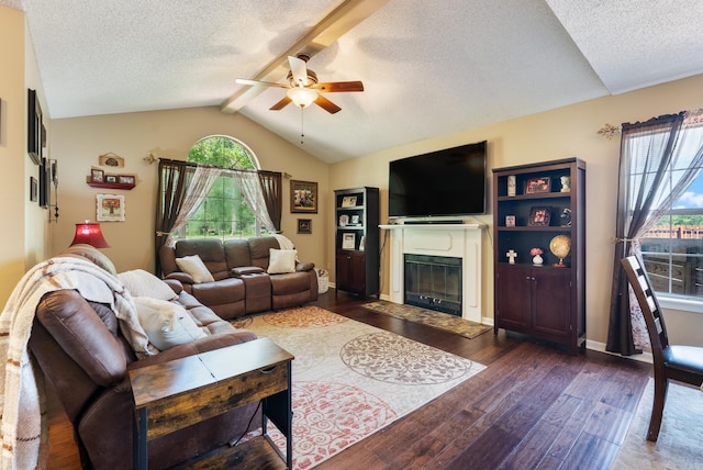 living area with dark wood finished floors, lofted ceiling with beams, ceiling fan, a glass covered fireplace, and a textured ceiling