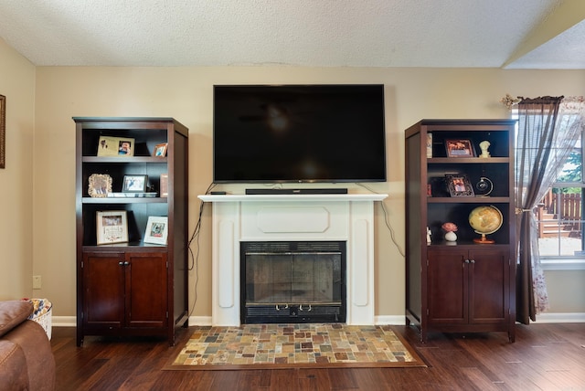 living area with dark wood-style floors, a textured ceiling, and a fireplace with flush hearth