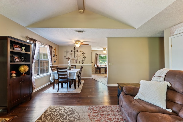 living area with lofted ceiling with beams, ceiling fan, visible vents, a textured ceiling, and dark wood-type flooring