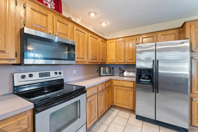 kitchen with brown cabinetry, stainless steel appliances, light tile patterned flooring, and light countertops