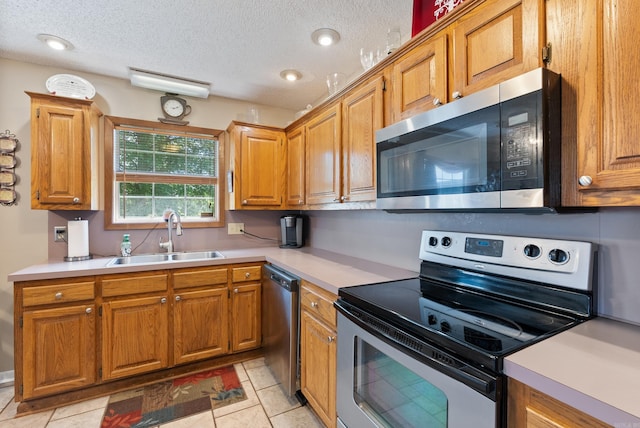 kitchen with brown cabinets, a sink, light countertops, a textured ceiling, and appliances with stainless steel finishes