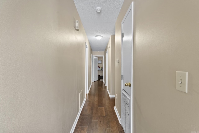 hallway with dark wood-style floors, baseboards, and a textured ceiling