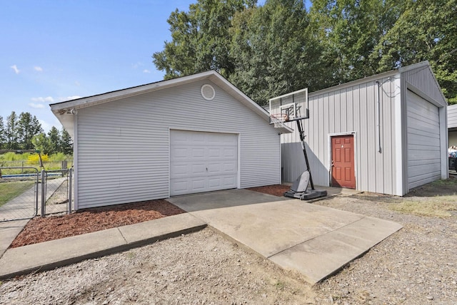 detached garage with driveway, fence, and a gate