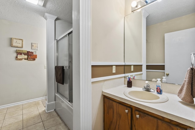 full bathroom featuring vanity, tile patterned floors, enclosed tub / shower combo, ornate columns, and a textured ceiling
