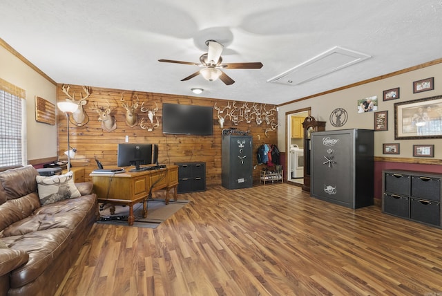 living area featuring attic access, a ceiling fan, wood walls, washer / clothes dryer, and wood finished floors