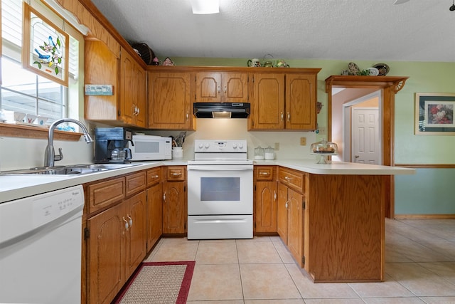 kitchen featuring white appliances, under cabinet range hood, light countertops, a sink, and a peninsula