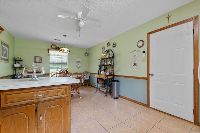 kitchen with light tile patterned floors, light countertops, brown cabinets, a ceiling fan, and a textured ceiling