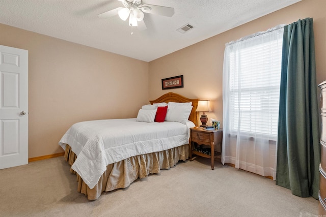 bedroom with a textured ceiling, light colored carpet, visible vents, ceiling fan, and baseboards