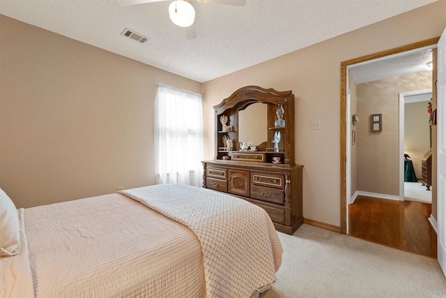 bedroom featuring a textured ceiling, visible vents, ceiling fan, baseboards, and light carpet