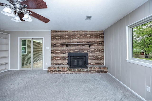 unfurnished living room featuring carpet flooring, a wood stove, visible vents, a ceiling fan, and built in shelves