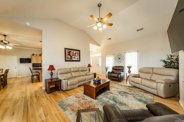 living area featuring lofted ceiling, visible vents, a ceiling fan, and light wood-style flooring