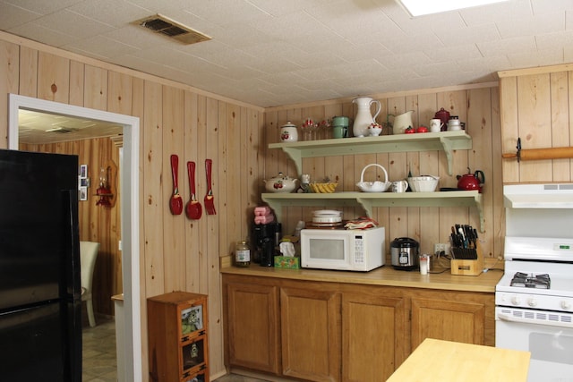 interior space with white appliances, open shelves, under cabinet range hood, wood walls, and visible vents