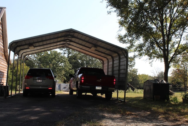 view of vehicle parking with driveway, a storage shed, and a carport