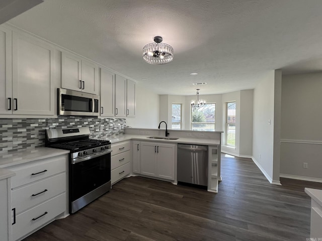 kitchen featuring a sink, appliances with stainless steel finishes, an inviting chandelier, a peninsula, and backsplash