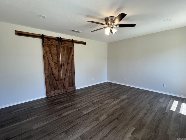 empty room featuring baseboards, a barn door, dark wood-style floors, visible vents, and a ceiling fan