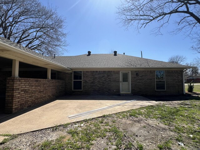 rear view of property with brick siding, a shingled roof, and a patio area