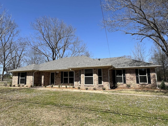 view of front of house with a front lawn, roof with shingles, and brick siding