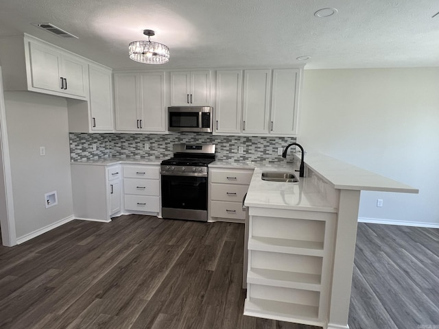 kitchen with a sink, appliances with stainless steel finishes, visible vents, dark wood-type flooring, and a peninsula