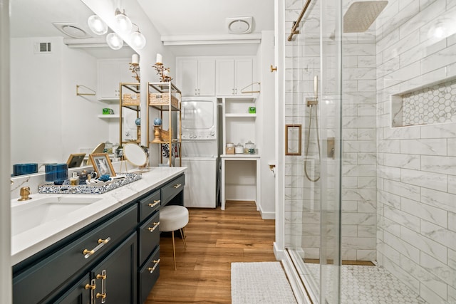 full bath with wood finished floors, a stall shower, vanity, visible vents, and stacked washer and clothes dryer