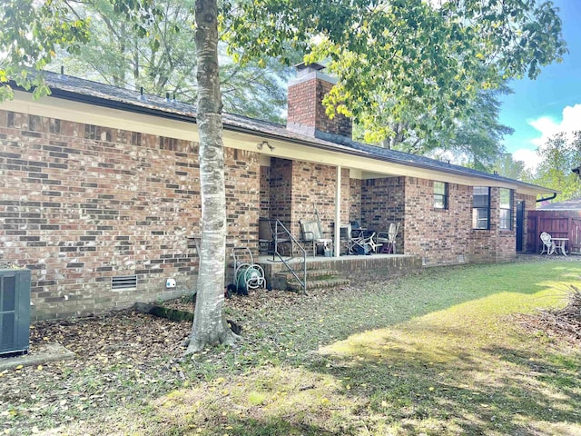 view of side of home featuring a chimney, a yard, brick siding, fence, and central AC unit