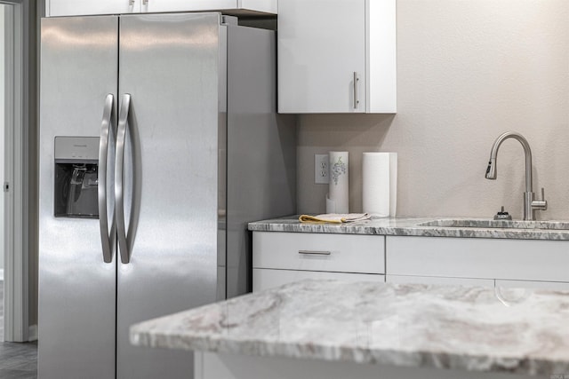 kitchen featuring light stone counters, a sink, white cabinets, and stainless steel fridge with ice dispenser