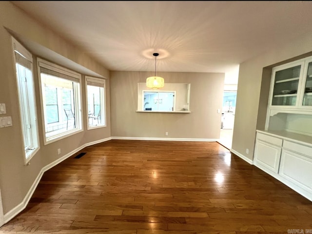 unfurnished dining area featuring baseboards, dark wood finished floors, and visible vents