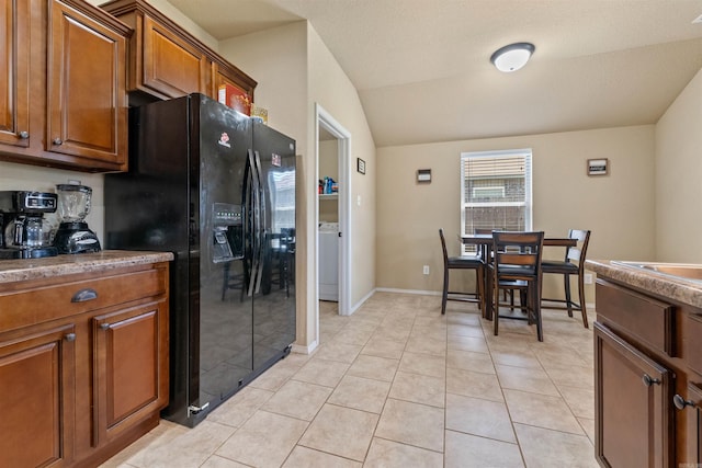 kitchen featuring light tile patterned flooring, brown cabinetry, lofted ceiling, and black fridge