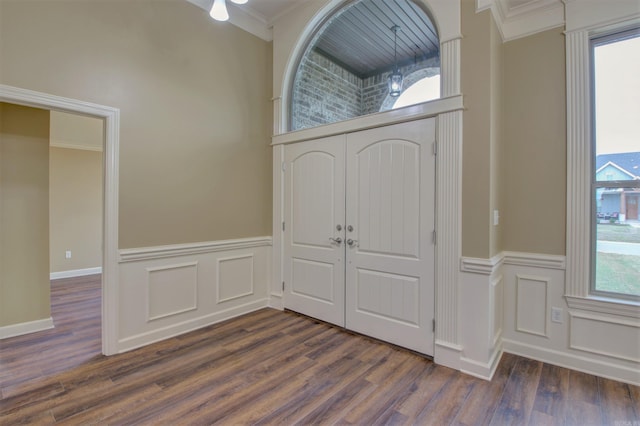 entrance foyer with crown molding, dark wood-style floors, and a wainscoted wall