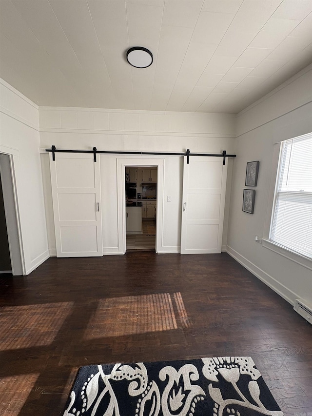 interior space with a barn door, dark wood-style floors, and baseboards