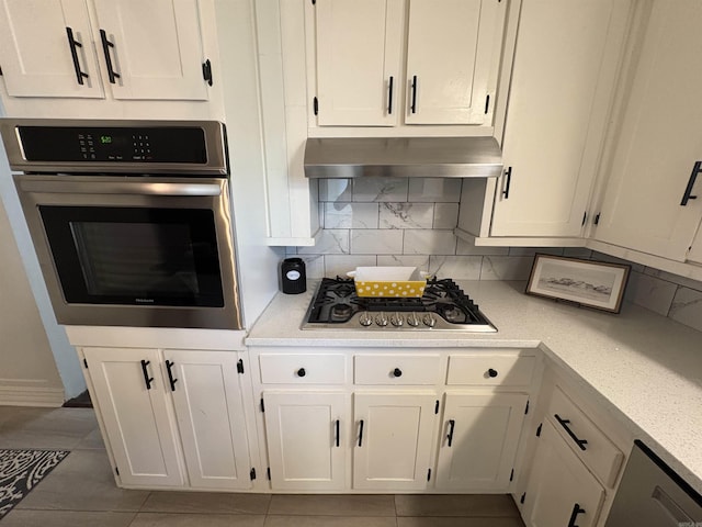 kitchen featuring decorative backsplash, under cabinet range hood, white cabinetry, light countertops, and appliances with stainless steel finishes