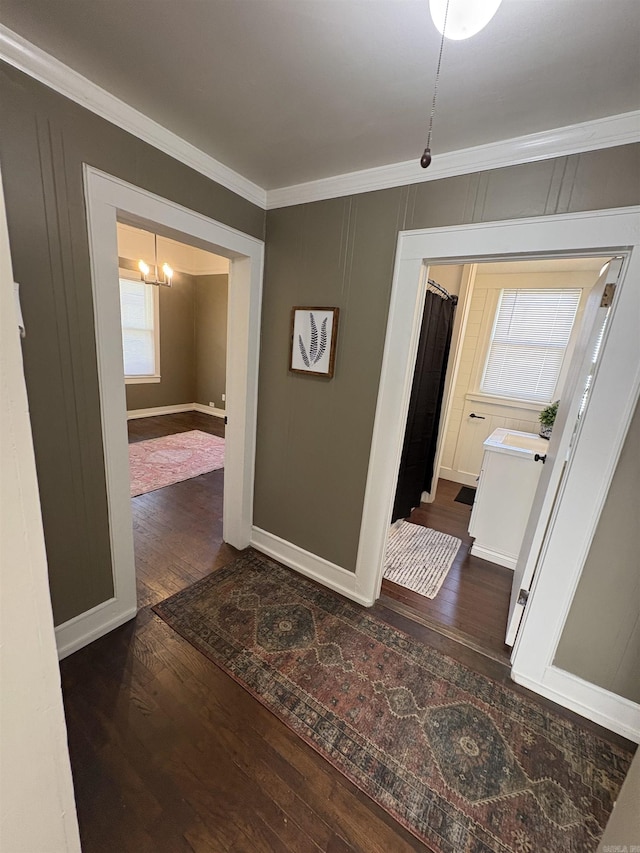 corridor with dark wood finished floors, baseboards, ornamental molding, and a notable chandelier