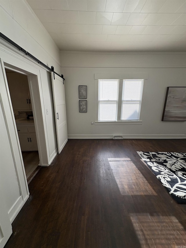 unfurnished bedroom with dark wood-style flooring, a barn door, visible vents, and baseboards