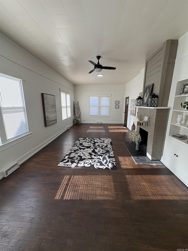 living area with a baseboard heating unit, ceiling fan, a fireplace, wood-type flooring, and baseboards
