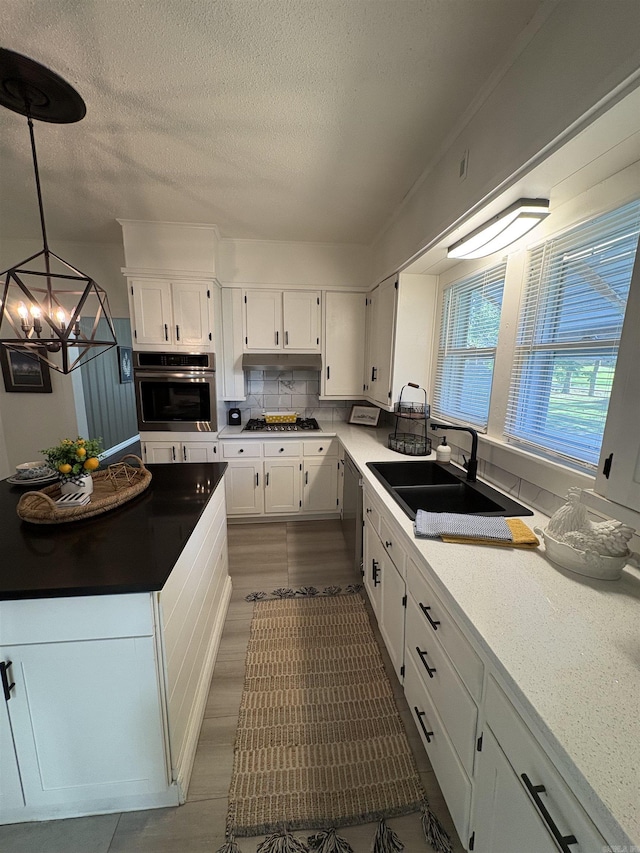 kitchen with a textured ceiling, white cabinets, a sink, appliances with stainless steel finishes, and a chandelier