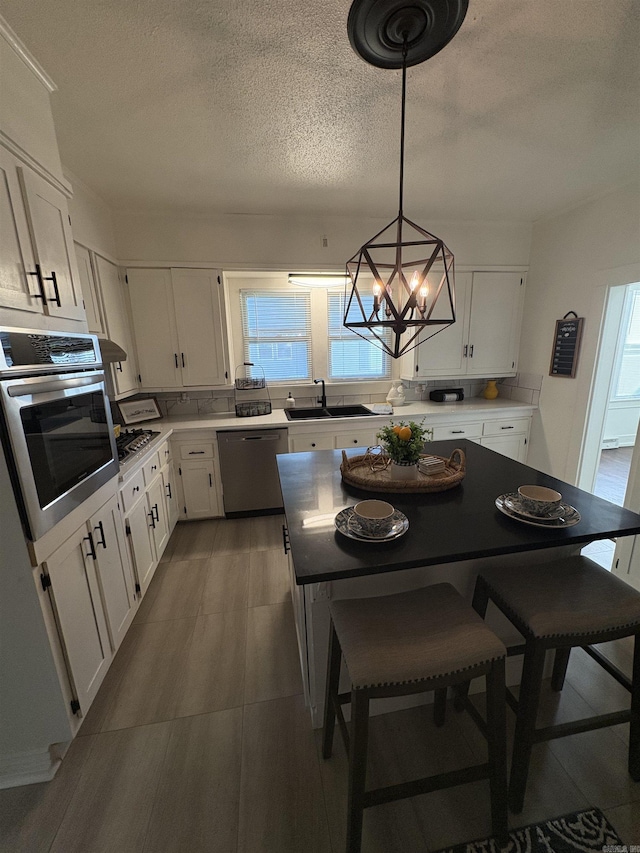 kitchen with a chandelier, appliances with stainless steel finishes, white cabinetry, and a sink
