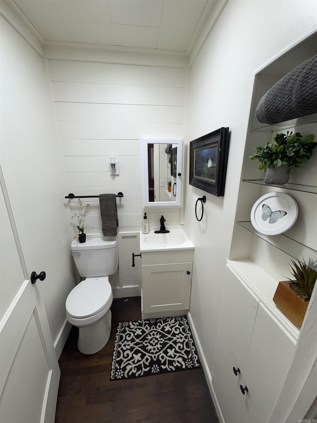 half bathroom with wood finished floors, toilet, vanity, baseboards, and wooden walls