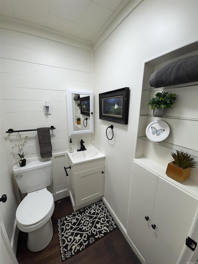 half bathroom featuring wood finished floors, toilet, vanity, and baseboards