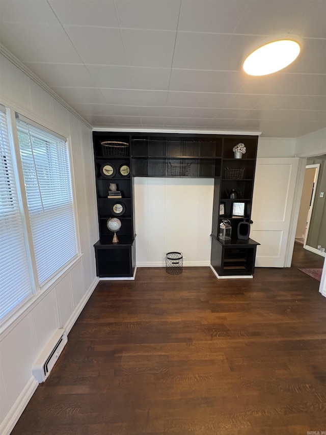 unfurnished living room with a decorative wall, crown molding, dark wood-style floors, and a baseboard heating unit