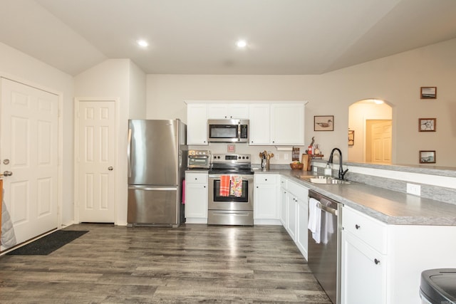 kitchen with arched walkways, appliances with stainless steel finishes, vaulted ceiling, a sink, and a peninsula