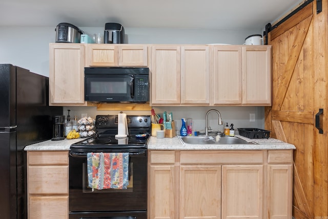 kitchen with light brown cabinetry, a barn door, light countertops, black appliances, and a sink
