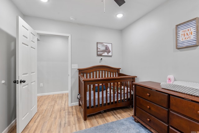 bedroom featuring baseboards, recessed lighting, a nursery area, and light wood finished floors