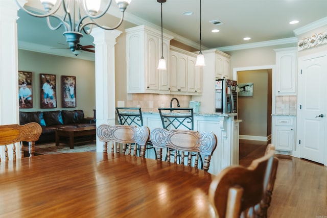 kitchen featuring light stone counters, decorative backsplash, refrigerator with ice dispenser, and decorative columns