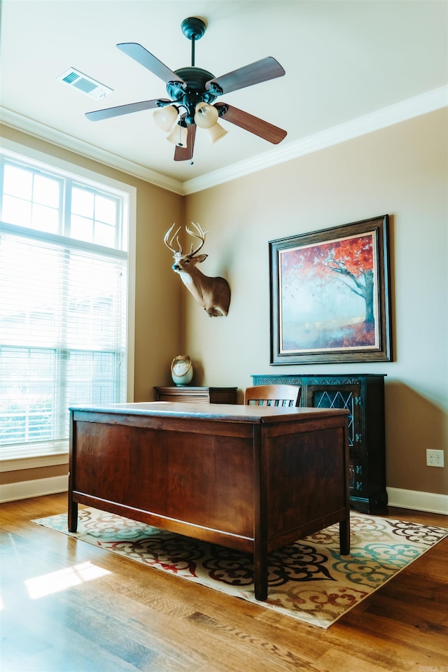 office space featuring wood finished floors, ornamental molding, baseboards, visible vents, and a ceiling fan