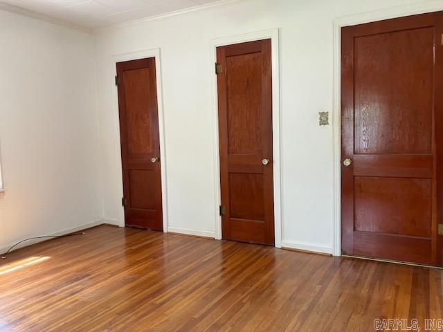 unfurnished bedroom featuring wood finished floors, crown molding, and baseboards