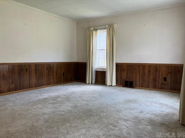 carpeted spare room with crown molding, visible vents, wainscoting, and wood walls