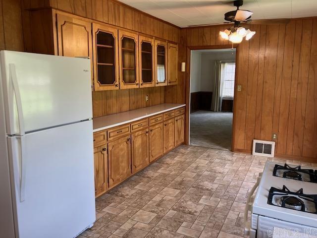 kitchen with white appliances, brown cabinetry, wooden walls, visible vents, and light countertops