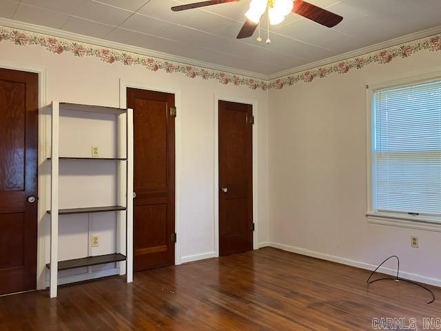 unfurnished bedroom with wood finished floors, crown molding, a ceiling fan, baseboards, and multiple closets