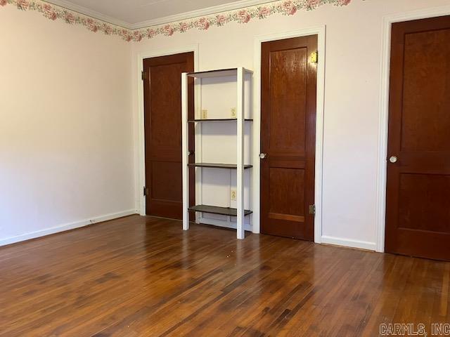 unfurnished bedroom with crown molding, baseboards, and dark wood finished floors